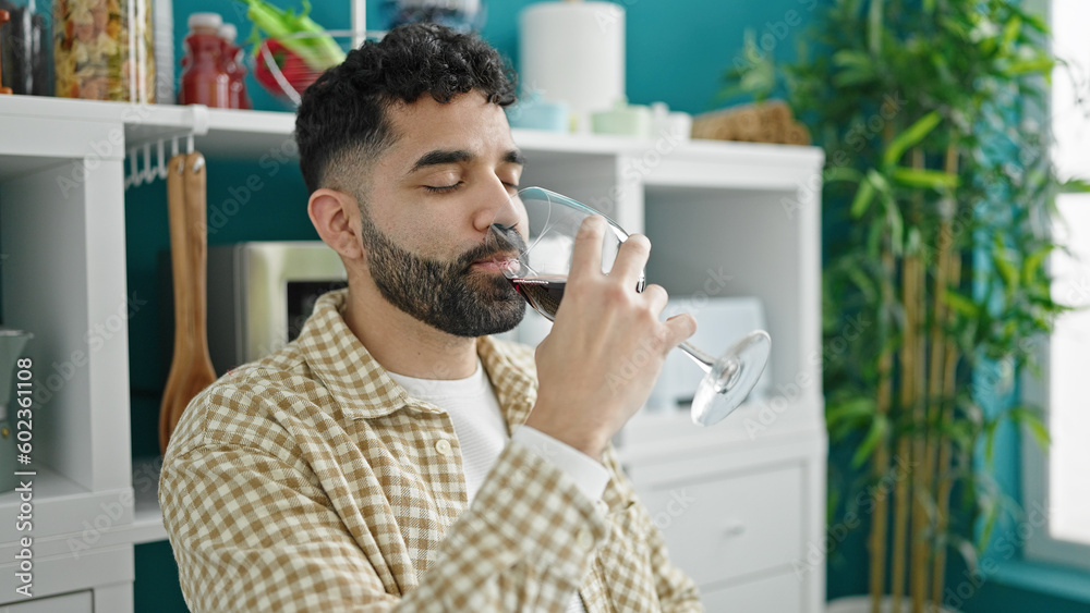 Young hispanic man drinking glass of wine sitting on table at dinning room