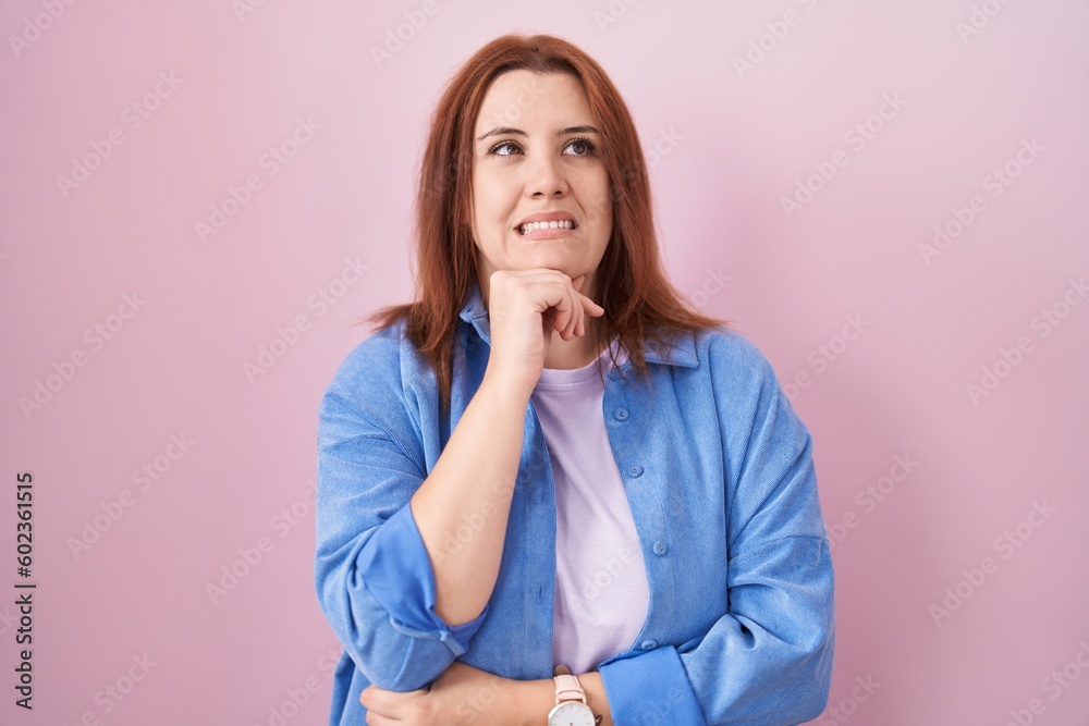 Young hispanic woman with red hair standing over pink background thinking worried about a question, concerned and nervous with hand on chin Young hispanic woman with red hair standing over pink background thinking worried about a question, concerned and nervous with hand on chin
