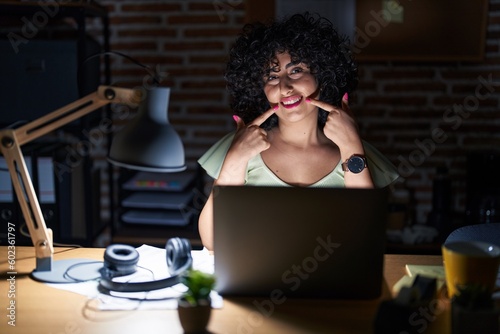 Young brunette woman with curly hair working at the office at night smiling cheerful showing and pointing with fingers teeth and mouth. dental health concept.