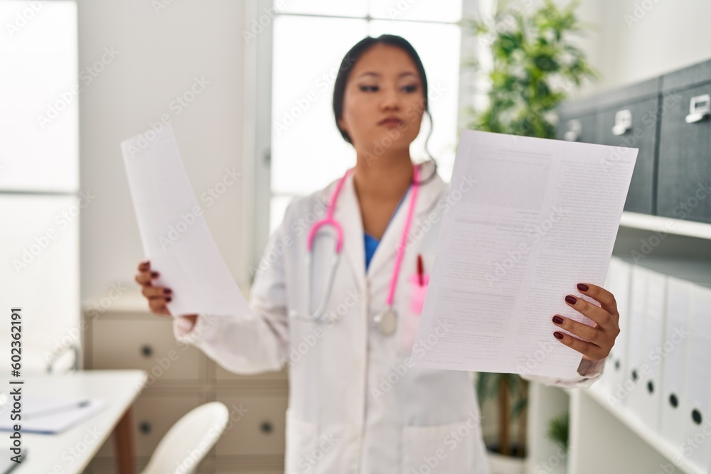 Young chinese woman wearing doctor uniform reading document at clinic Young chinese woman wearing doctor uniform reading document at clinic