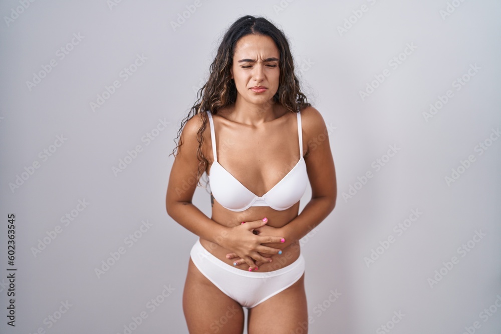 Young hispanic woman wearing white lingerie with hand on stomach because indigestion, painful illness feeling unwell. ache concept.