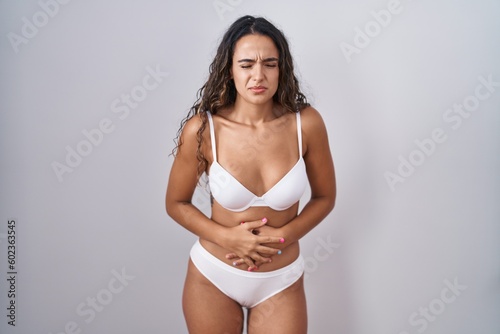 Young hispanic woman wearing white lingerie with hand on stomach because indigestion, painful illness feeling unwell. ache concept. © Krakenimages.com