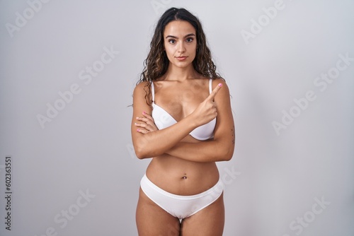 Young hispanic woman wearing white lingerie pointing with hand finger to the side showing advertisement, serious and calm face © Krakenimages.com