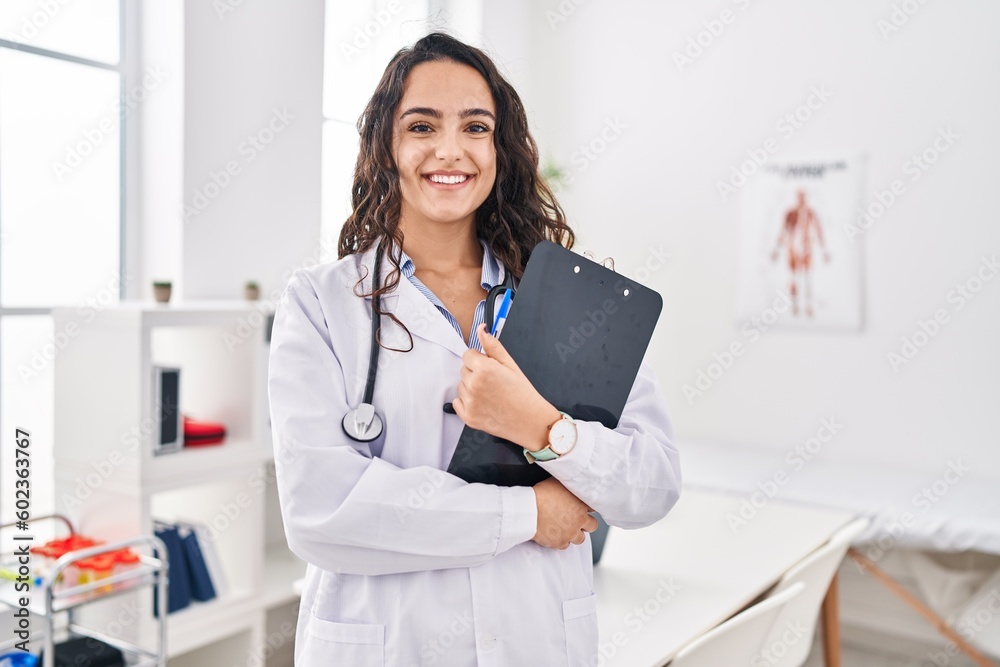 Young hispanic woman wearing doctor uniform holding clipboard at clinic Young hispanic woman wearing doctor uniform holding clipboard at clinic