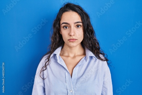 Young brunette woman standing over blue background depressed and worry for distress, crying angry and afraid. sad expression.