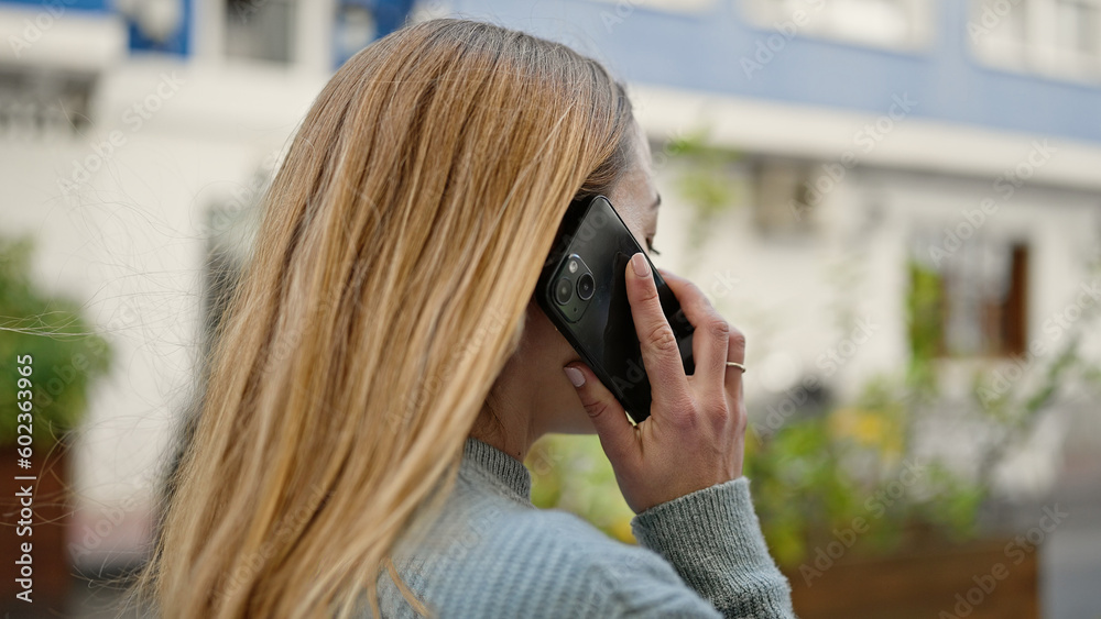 Young blonde woman talking on the smartphone at street