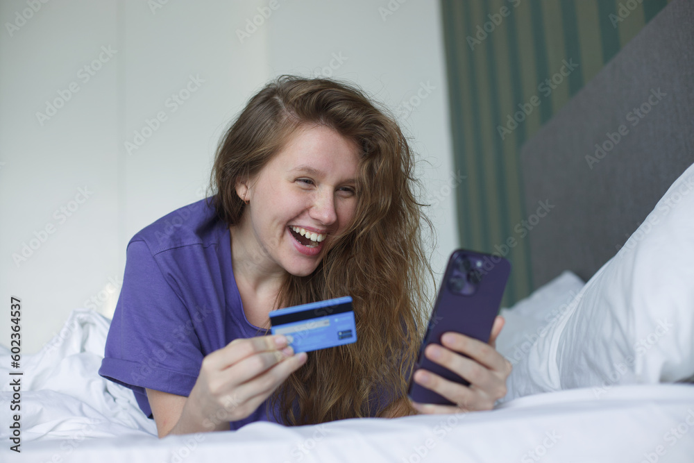Portrait of happy excited amazed girl, shocked young successful joyful woman paying, holding credit bank card with phone, laptop celebrating victory, triumph, success at home. Online shopping Portrait of happy excited amazed girl, shocked young successful joyful woman paying, holding credit bank card with phone, laptop celebrating victory, triumph, success at home. Online shopping