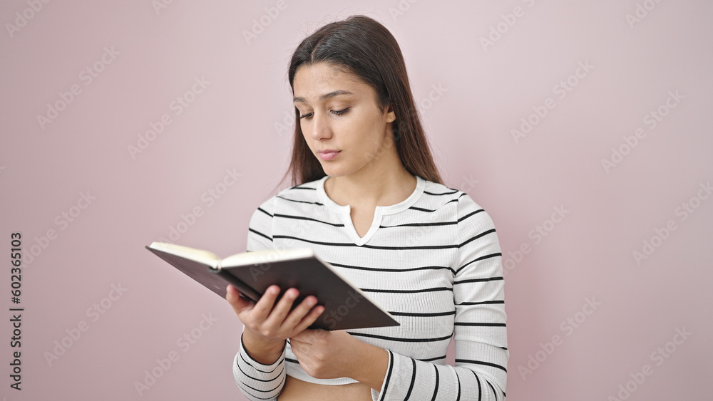 Young beautiful hispanic woman reading book over isolated pink background Young beautiful hispanic woman reading book over isolated pink background