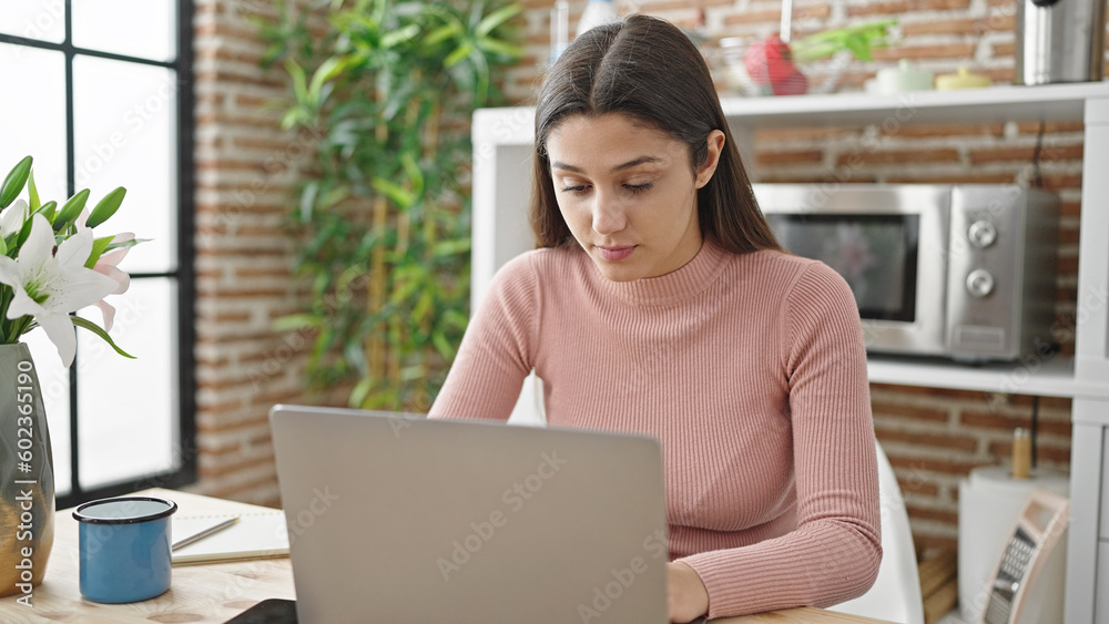 Young beautiful hispanic woman using laptop sitting on table at dinning room Young beautiful hispanic woman using laptop sitting on table at dinning room