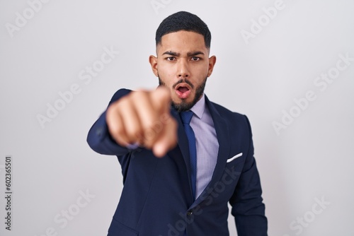 Young hispanic man wearing business suit and tie pointing displeased and frustrated to the camera, angry and furious with you