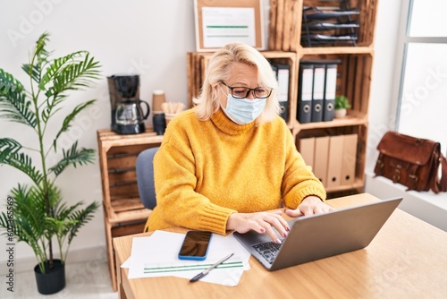 Middle age blonde woman business worker wearing medical mask working at office