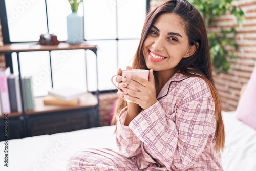 Young beautiful arab woman drinking cup of coffee sitting on bed at bedroom