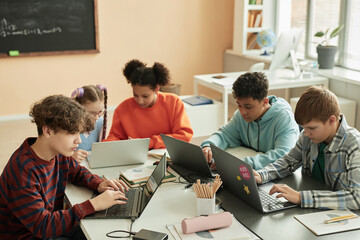 High angle view at diverse group of teen schoolchildren using computers in classroom studying together