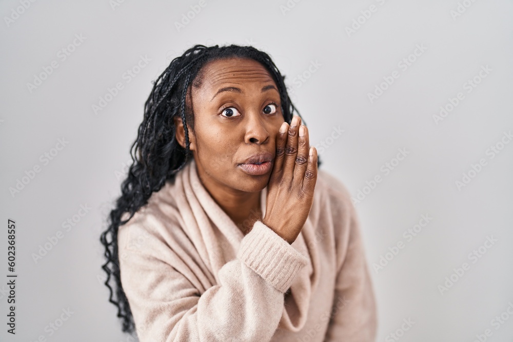 African woman standing over white background hand on mouth telling secret rumor, whispering malicious talk conversation - obrazy, fototapety, plakaty 