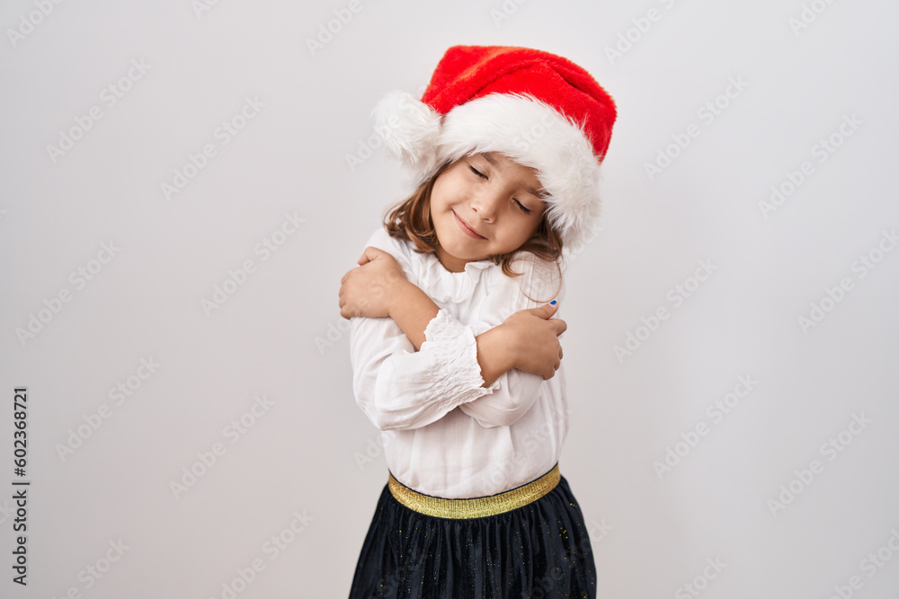 Little hispanic girl wearing christmas hat hugging oneself happy and positive, smiling confident. self love and self care Little hispanic girl wearing christmas hat hugging oneself happy and positive, smiling confident. self love and self care