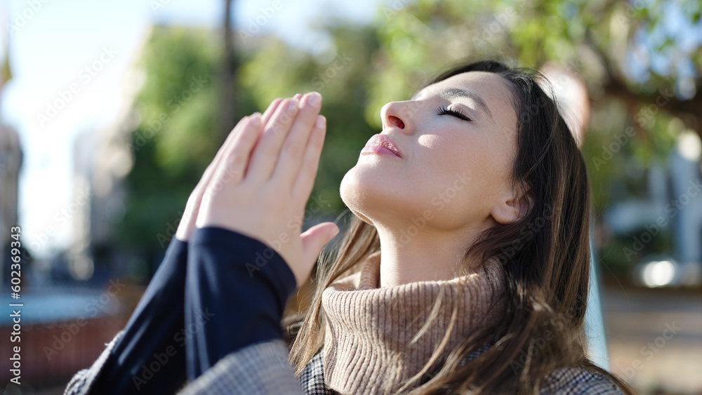 Beautiful hispanic woman praying with closed eyes at park