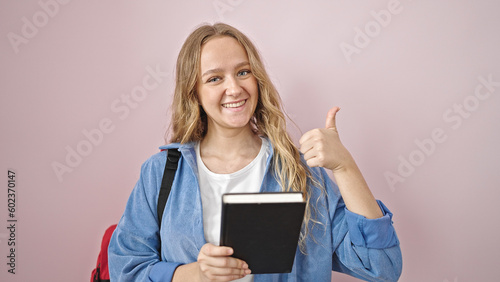 Young blonde woman student reading book doing thumb up gesture over isolated pink background