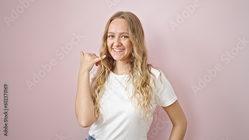 Young blonde woman smiling confident doing call me gesture with hand over isolated pink background