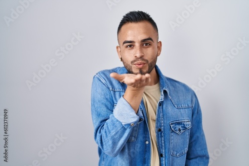 Young hispanic man standing over isolated background looking at the camera blowing a kiss with hand on air being lovely and sexy. love expression.