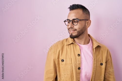 Young hispanic man standing over pink background looking away to side with smile on face, natural expression. laughing confident. © Krakenimages.com