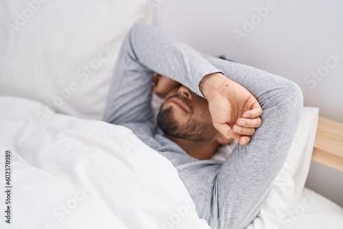 Young hispanic man lying on bed crying at bedroom