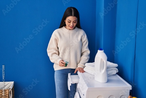 Young beautiful hispanic woman smiling confident pouring detergent on washing machine at laundry room