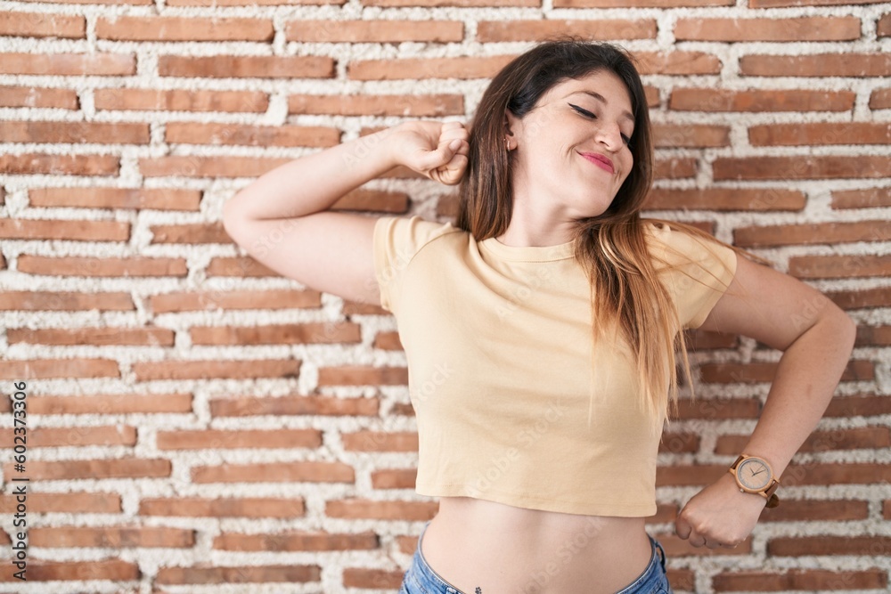 Young brunette woman standing over bricks wall stretching back, tired and relaxed, sleepy and yawning for early morning Young brunette woman standing over bricks wall stretching back, tired and relaxed, sleepy and yawning for early morning