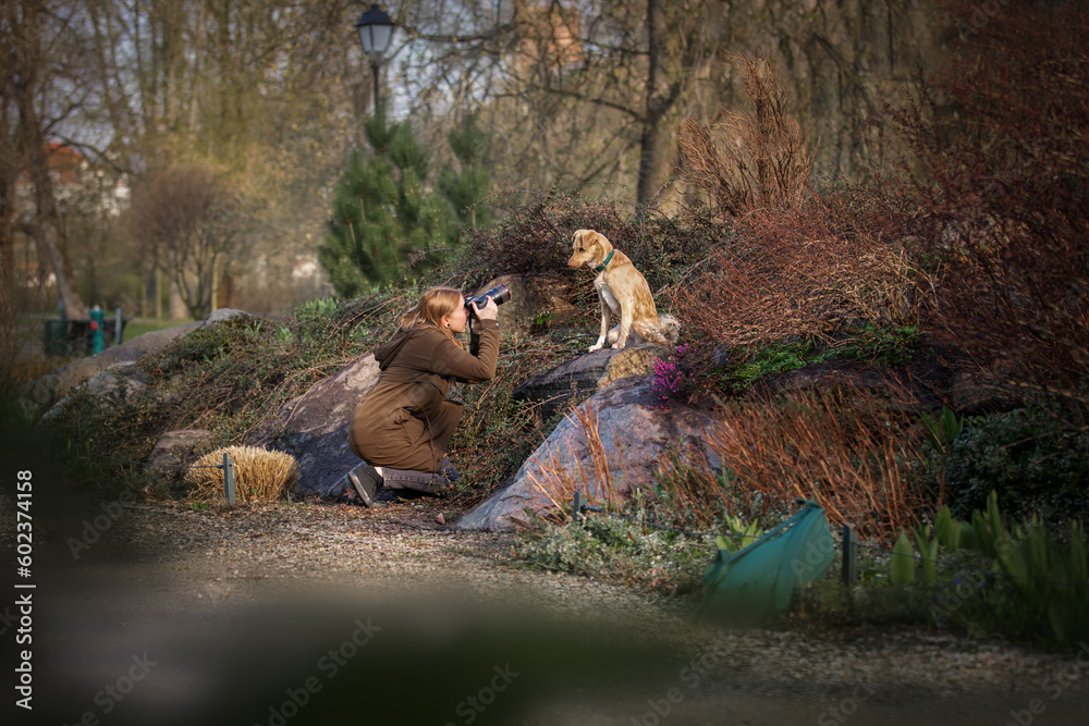 Beautiful blonde girl photographs dog in the park