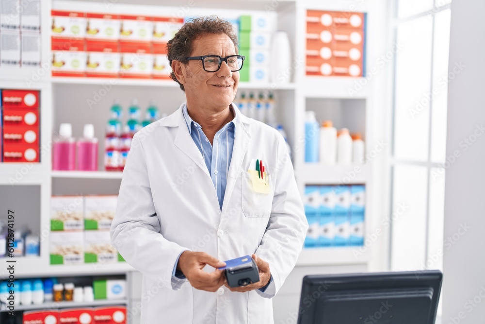 Middle age man pharmacist using credit card and data phone at pharmacy