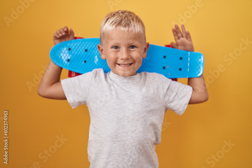 Little caucasian boy holding skate smiling with a happy and cool smile on face. showing teeth.