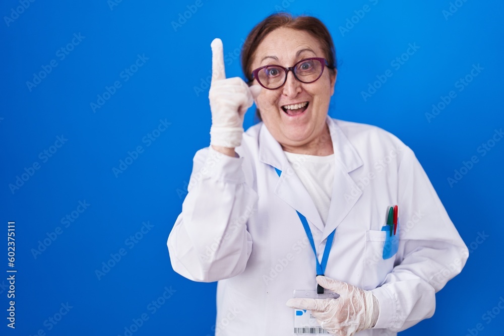 Senior woman with glasses wearing scientist uniform pointing finger up with successful idea. exited and happy. number one. Senior woman with glasses wearing scientist uniform pointing finger up with successful idea. exited and happy. number one.