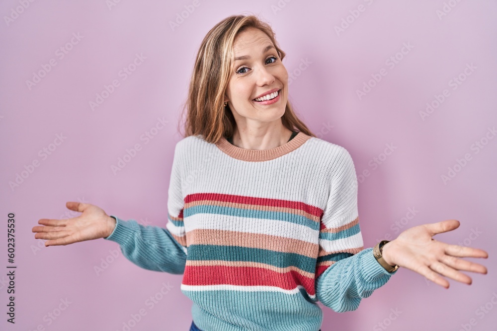 Young blonde woman standing over pink background smiling cheerful with open arms as friendly welcome, positive and confident greetings