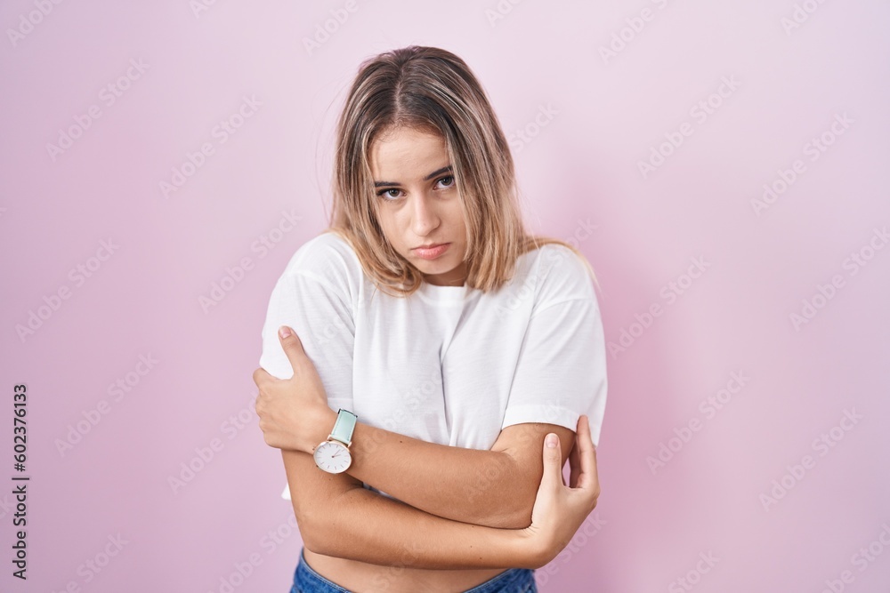Obraz premium Young blonde woman standing over pink background shaking and freezing for winter cold with sad and shock expression on face