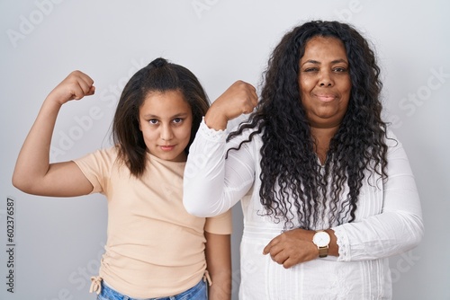 Mother and young daughter standing over white background strong person showing arm muscle  confident and proud of power