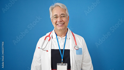 Middle age man with grey hair doctor smiling confident standing over isolated blue background