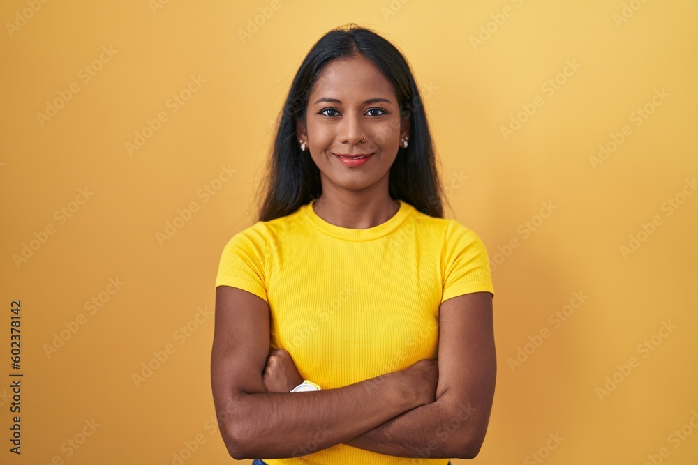 Obraz premium Young indian woman standing over yellow background happy face smiling with crossed arms looking at the camera. positive person.