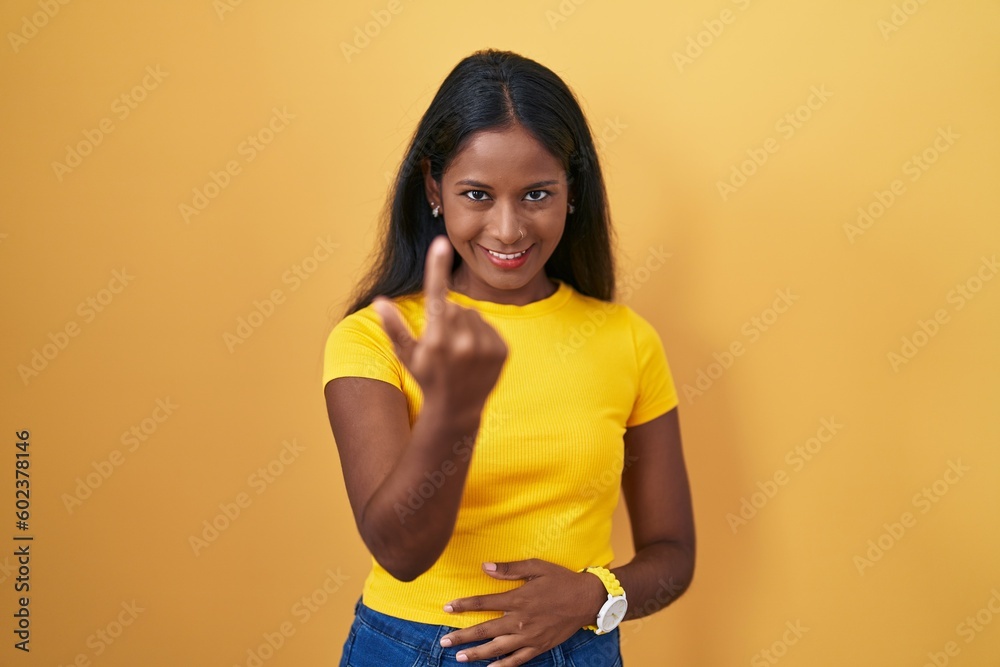 Young indian woman standing over yellow background beckoning come here gesture with hand inviting welcoming happy and smiling Young indian woman standing over yellow background beckoning come here gesture with hand inviting welcoming happy and smiling