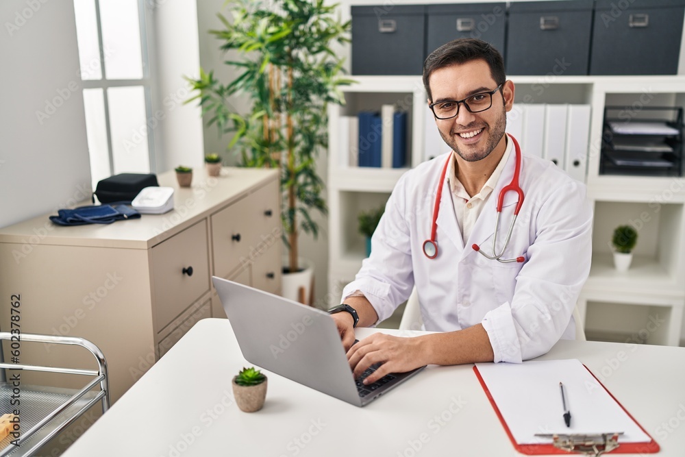 Young hispanic man wearing doctor uniform using laptop working at clinic Young hispanic man wearing doctor uniform using laptop working at clinic