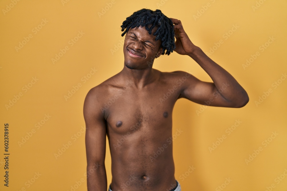 Fototapeta premium Young african man with dreadlocks standing shirtless confuse and wonder about question. uncertain with doubt, thinking with hand on head. pensive concept.