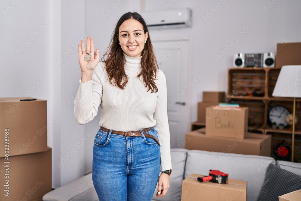 Young hispanic woman holding keys of new home looking positive and happy standing and smiling with a confident smile showing teeth Young hispanic woman holding keys of new home looking positive and happy standing and smiling with a confident smile showing teeth