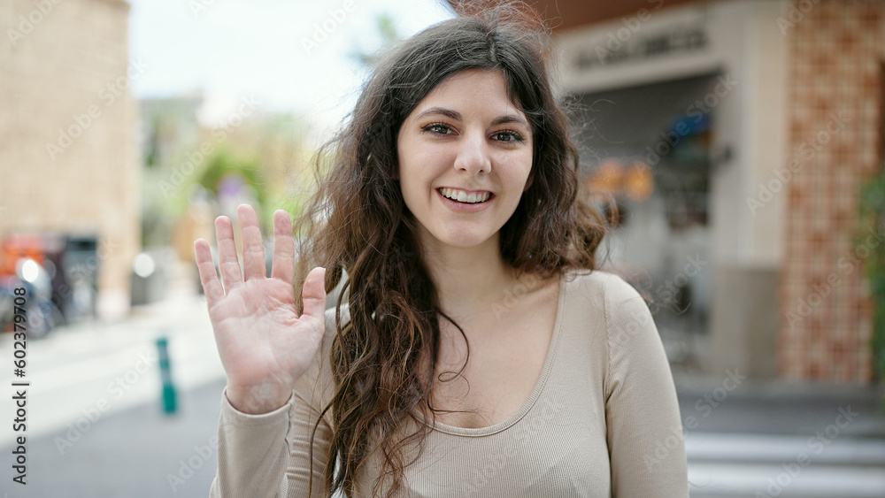 Young beautiful hispanic woman smiling confident saying hello with hand at street