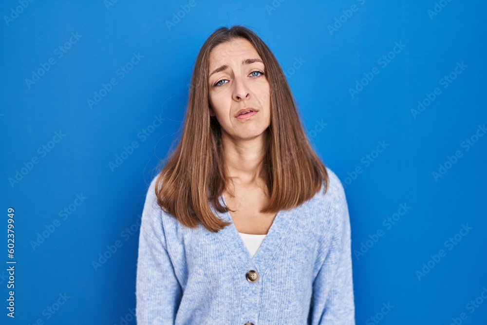 Fototapeta premium Young woman standing over blue background looking sleepy and tired, exhausted for fatigue and hangover, lazy eyes in the morning.