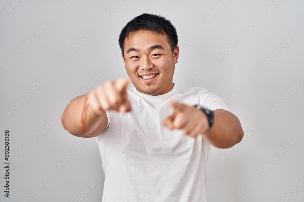 Young chinese man standing over white background pointing to you and the camera with fingers, smiling positive and cheerful Young chinese man standing over white background pointing to you and the camera with fingers, smiling positive and cheerful