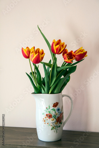 A white porcelain jug with flower print containing a bouquet of red and yellow tulips