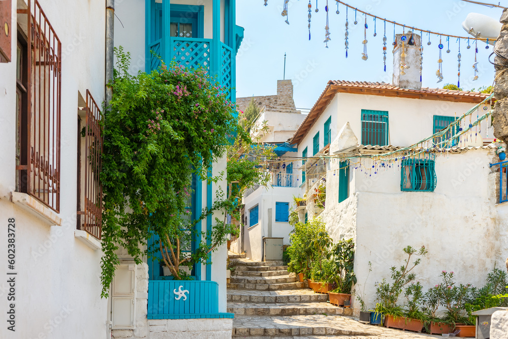 Narrow street in old european town in summer sunny day. Beautiful scenic old ancient white houses, cafe and shops with green plants. Popular tourist vacation destination, mediterranean architecture