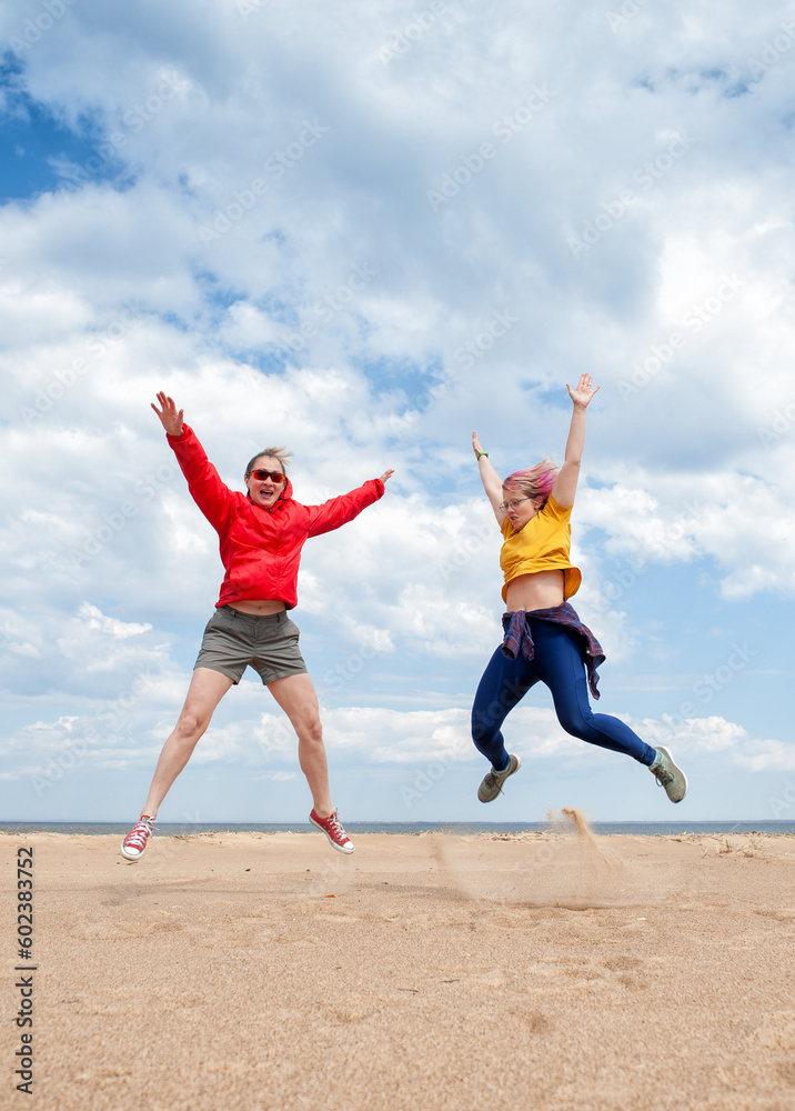 Two cheerful women having fun and jumping on the sand