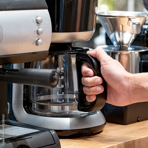 Buying a coffee machine for home appliances. Male hand holding glass pot on coffee maker in barista tool shop.