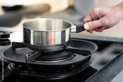 Shopping kitchen utensils concept. Male hand holding stainless steel saucepan on gas stove in kitchenware showroom store. Buying cookware for the domestic kitchen at home.