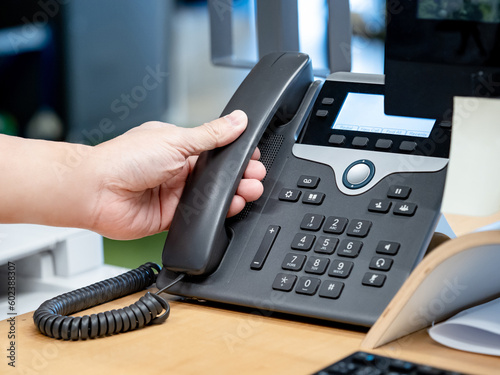 Call center and customer support. Operator hand trying to response customer call by using landline VoIP phone on help desk in the office.