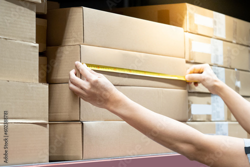 Male worker hands using tape measure on carton box in warehouse. Checking dimensions for goods delivery. Logistics service and cargo shipping business concepts © Summer Paradive